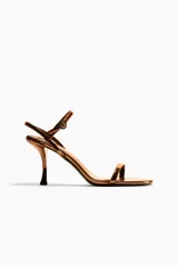 Sandalias de tacón alto fino con acabado metalizado dorado, diseño de tiras finas y tira ajustable al tobillo con hebilla.