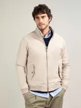 Campera Harrington color beige, con cuello alto abotonado, cierre frontal completo y bolsillos laterales con solapa y botones a presión. Puños y cintura elastizados de rib.