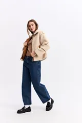 Campera tipo teddy de textura suave y acabado de peluche en color beige. Presenta cuello amplio con detalle de hebilla, cierre frontal y recortes en contraste de color marrón que marcan la estructura de la prenda.