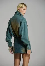 Falda mini de denim color azul con efecto deslavado en tonos amarronados y aplicación de brillos en toda la superficie. Cuenta con tiro medio, bolsillos delanteros y traseros, y cierre frontal con botones metálicos.