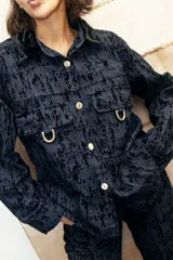 Camisa recta de gabardina con efecto "roto", que aporta volumen y textura. Presenta bolsillos amplios con solapa en el frente adornados con mini estribos dorados y cierre frontal de botones.