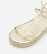 Sandalia plana tipo flatform de color dorado, con tiras finas en diseño Salomé y suela con detalle de yute trenzado.
