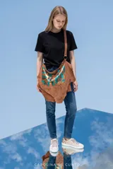 Cartera bandolera de cuero natural de gran tamaño, color marrón con detalles pintados a mano en tonos turquesa y dorado. Presenta silueta orgánica y caída irregular, con correa regulable y bolsillo posterior con cierre.