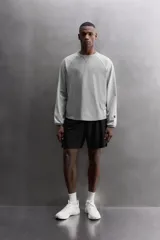 Camiseta de algodón gris de corte relajado con mangas largas ranglán de color gris más claro y puños elásticos. Presenta un pequeño bordado en el pecho y un parche con logo en la parte inferior delantera.