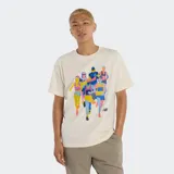 Remera de manga corta color crema con un estampado gráfico de corredores en colores vibrantes (amarillo, azul, rosa, celeste). Incluye el logo de New Balance en la parte inferior del estampado.