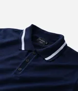 Remera polo azul marino de media malla con cuello y bajo a rayas blancas. Tiene cuello abotonado y mangas cortas.