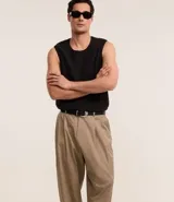 Pantalón de vestir color beige, de corte amplio estilo japonés, con cintura con trabillas, cierre tradicional, pliegues frontales, bolsillos laterales y traseros, y efecto satinado.