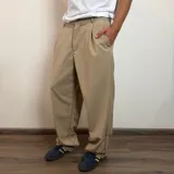 Pantalón sastrero color beige, de corte baggy, con pliegues en la cintura y bolsillos laterales.