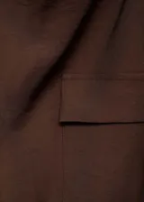 Blusa marrón sin mangas con cuello drapeado, trabillas, dos bolsillos de solapa en el pecho y cinturón desmontable. Cierre de botón en la parte posterior y diseño recto.