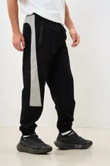 Pantalón negro de corte deportivo con cintura elástica y cordón ajustable. Presenta una franja vertical gris a lo largo de la pierna y puños elásticos.