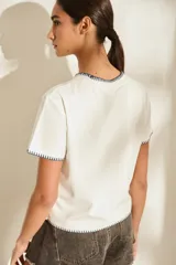 Remera marrón de manga corta y cuello redondo, con detalles de costuras decorativas en contraste color crudo en el cuello, los puños y el dobladillo inferior. Cuenta con el nombre de la marca impreso en el pecho.