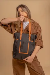 Bolso tipo tote bag de símil cuero color rosa pálido, con asas dobles y detalles de costura en color beige claro. Presenta un bolsillo frontal rectangular aplicado y herrajes metálicos.