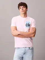 Remera rosada de manga corta con cuello redondo y corte regular, confeccionada en algodón regenerativo. Cuenta con un estampado gráfico en caja de color celeste con el monograma "ck" en negro en el pecho.