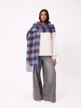 Bufanda de tejido suave con diseño de cuadros grandes en tonos naranja, rojo, violeta y lila. Presenta flecos en los extremos y una etiqueta pequeña con el logo de la marca Rusty.