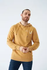 Buzo canguro color mostaza con capucha ajustable mediante cordones, bolsillo frontal tipo canguro y estampado gráfico en el pecho. Presenta puños y ruedo acanalados.