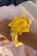 Coletero amarillo tejido a crochet con forma de sol y elástico con estampado a rayas amarillas y blancas.