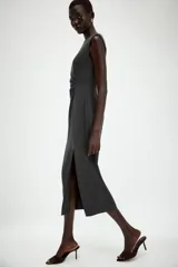 Vestido midi sin mangas de cuello redondo, con detalle de drapeado en el delantero y abertura frontal en el bajo. Cierre posterior con cremallera oculta.