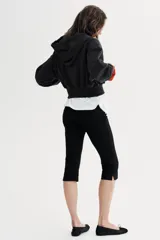 Sudadera negra con capucha, cierre frontal de cremallera metálica y mangas largas con puños. Presenta un diseño corto con bolsillo tipo canguro y detalle de texto 'California' aplicado con brillos en el frente.