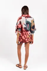 Vestido camisero oversize de tela calada con estampado abstracto multicolor, cuello camisero, mangas anchas y lazo ajustable en la cintura confeccionado en la misma tela.