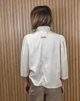 Camisa de algodón color blanco, con cuello alto con volados, mangas tres cuartos con detalles de bordado ingles y cierre frontal con botones de nácar.