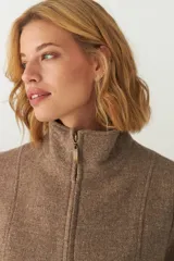 Campera de lana fina sin teñir, con cuello alto, cierre frontal completo y diseño de corte recto con pespuntes decorativos en puños, ruedo y cuello.