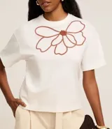 Blusa boxy de mangas cortas color blanco, confeccionada en algodón, con cuello redondo y bordado floral en el frente.