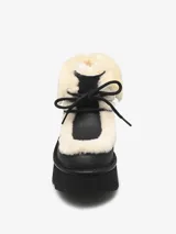 Bota de cuero negro con plataforma robusta y taco medio. Presenta detalles de piel de oveja en el borde superior y la lengüeta, con sistema de ajuste mediante cordones negros.