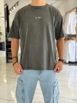 Remera oversize de color gris con efecto gastado (acid wash). Presenta un diseño de tipografía en la parte frontal y un gran estampado en la espalda con la inscripción "Create Bigger". Cuenta con mangas cortas y un calce holgado y cómodo.