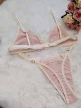 Conjunto de lencería compuesto por un bralette triangular y una tanga, confeccionados en algodón color rosado con detalles de encaje en tono crema. El bralette cuenta con breteles ajustables y el conjunto presenta terminaciones delicadas.