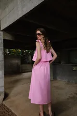 Vestido midi de color rosado con escote recto elástico y tirantes anchos con lazos ajustables. Presenta cintura elástica y bolsillos laterales ocultos en la costura.