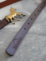 Cinturón de cuero color marrón chocolate con hebilla metálica en forma de caballo.