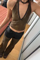 Top marrón de cuero ovino vintage con cuello halter y espalda descubierta. Presenta detalle artesanal de cutouts y pasamanería en negro alrededor del cuello y lazos finos negros para atar en el frente.