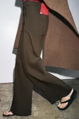 Capa de punto color marrón, con escote en V, mangas cortas y bolsillos de plastrón en el delantero. El ruedo tiene un corte asimétrico.