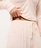 Pantalón de pijama tipo jogger confeccionado en viscolycra, con cintura elástica, cordón de ajuste y botamangas ajustadas. Presenta un estampado de perritos sobre una base de color rosado claro.