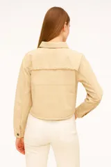 Sobrecamisa de denim en color gris lavado, con corte cropped, cuello clásico y cierre frontal mediante botones metálicos. Presenta costuras horizontales decorativas en el pecho y mangas largas con puños abotonados.