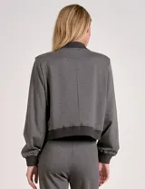 Camperita tipo bomber color beige claro, con cuello redondo acanalado, cierre frontal con broches metálicos y bolsillos delanteros con tapa. Los puños y el bajo son acanalados.