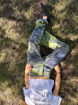 Pantalon de tiro medio y corte recto, confeccionado en tela con textura marcada y acabado rustico. Presenta un estampado artesanal con variaciones de tonos tierra y marrones, evocando un aspecto desgastado y natural.