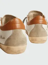 Zapatillas Golden Goose modelo Super Star, color blanco con estrella de gamuza gris, talón de cuero marrón y suela gastada.