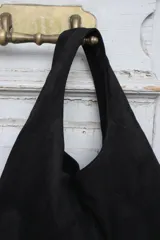 Cartera tipo hobo de gamuza negra, con diseño minimalista y asa integrada.