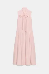 Vestido midi de Zara Woman Collection color rosado, confeccionado en hilatura de algodón. Presenta cuello subido con lazada, diseño sin mangas, bolsillos laterales ocultos y pliegues delanteros. Su falda tiene acabado en línea evasé y cuenta con cierre frontal mediante botones ocultos por solapa.