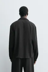 Camisa de corte relajado confeccionada en tejido fluido con mezcla de viscosa. Presenta diseño de rayas verticales sutiles, cuello con solapas de muesca, manga larga con puños abotonados y cierre frontal de botonadura cruzada.