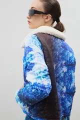 Campera con estampado de bosque en tonos azules, cuello de sherpa en color crema y cierre frontal con cremallera. Cuenta con elástico ajustable en la cintura.