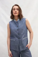 Chaleco azul de lino con cuello mao, abotonado al frente y bolsillos ojal con ribete blanco.