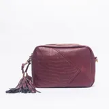 Bandolera de cuero sintético color bordó, con diseño combinado de textura lisa y efecto croco. Cuenta con cierre superior metálico y un detalle de borla decorativa en el lateral.