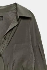 Camisa de corte amplio y fluido con cuello solapa, manga larga con puños abotonados y bolsillo de plastrón en el delantero. Presenta cierre frontal con botones y un acabado satinado.