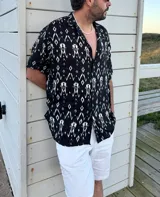 Camisa negra con estampado abstracto en blanco, de manga corta y cuello clásico.