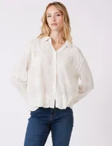 Camisa de algodón color blanco, con cuello con solapa y abertura central con botones. Presenta bordados de mariposas en las mangas y diseños florales en el frente y el dobladillo.