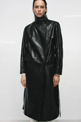 Trench de corte largo confeccionado en piel 100% con acabado brillante. Presenta cuello alto, hombreras marcadas, manga larga, bolsillos con solapa en el delantero y cierre frontal con botones. Incluye un cinturón ajustable del mismo material para entallar la silueta.