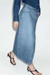 Falda midi de denim azul con diseño cruzado, cierre frontal con botones metálicos y bolsillos delanteros.