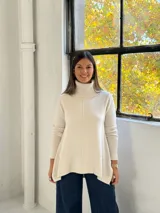 Sweater de punto color beige con cuello alto tipo polera, diseño holgado y costuras visibles en el frente.